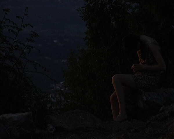 Still from Litania by Diego Marcon: a girl sitting on rocks at night, barely visible in the dark